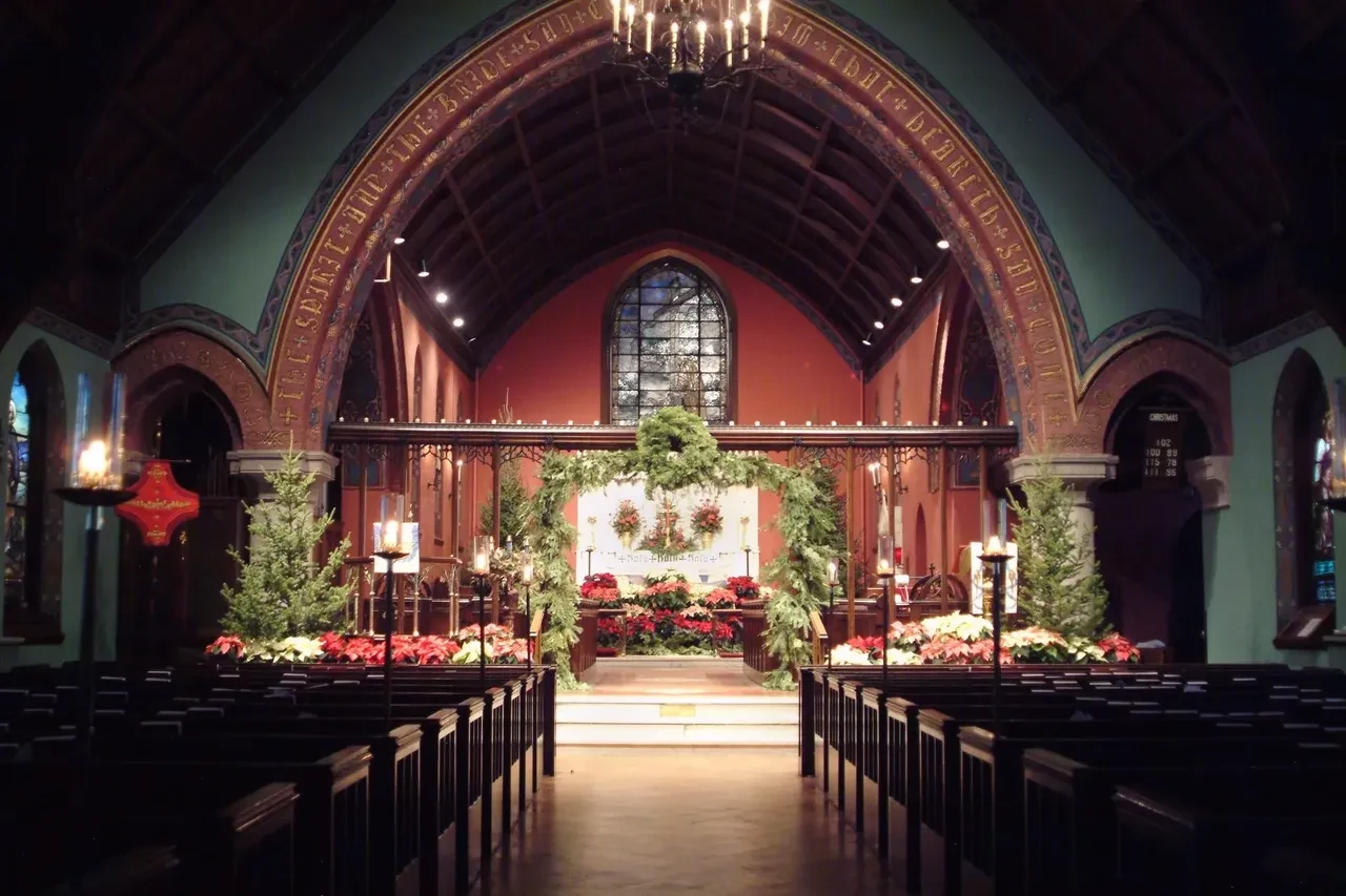 Church interior decorated with Christmas poinsettias, garlands, and candlelight