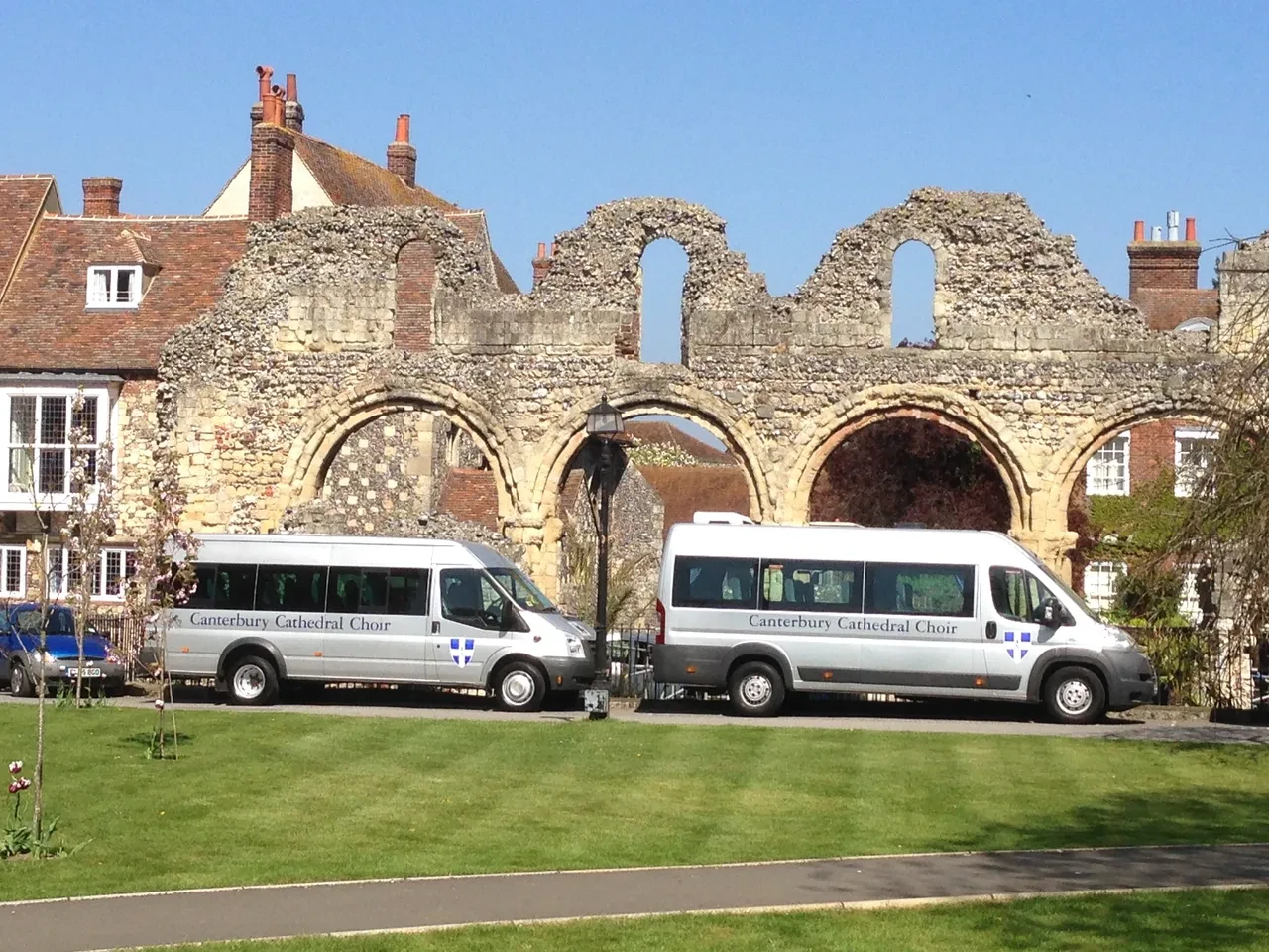Canterbury Cathedral Choir vans parked before historic stone ruins